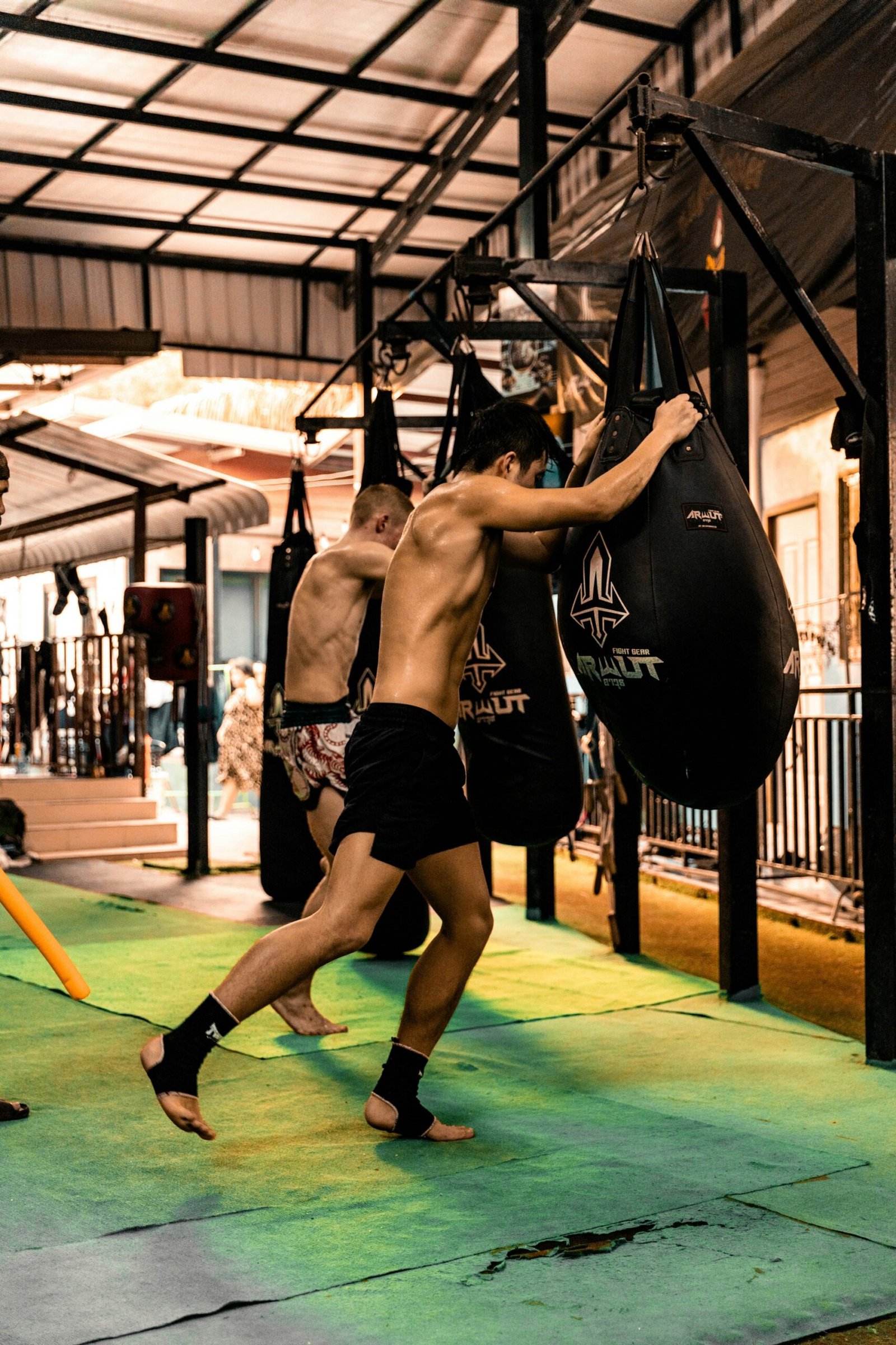 People sharing training space at heavy bags in a boxing gym.