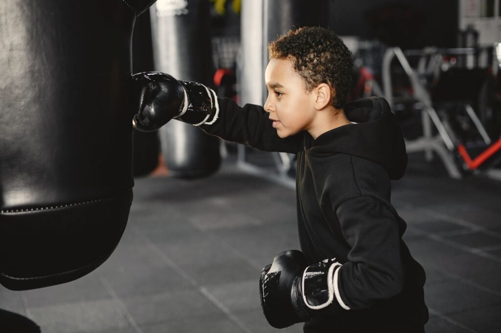 Young boxer practicing a controlled punch on a heavy bag while learning in a gym.